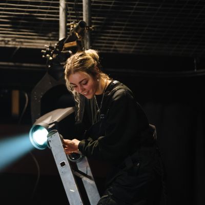 Lighting student up a ladder working on a light